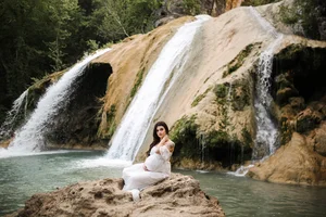 Maternity photo in white dress by waterfall in Texas